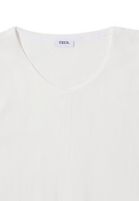 Blusa blanca con escote en V y textura acanalada. La etiqueta "CECIL" es visible en el cuello. Diseño simple sin patrones ni acentos adicionales.