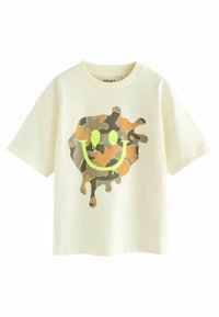 Cream-colored T-shirt with a loose fit. Features a camouflage smiley face design in shades of green and brown, with drip effects.