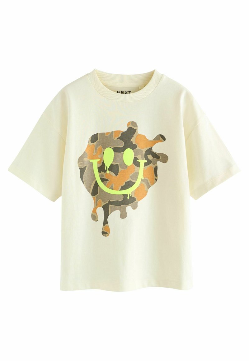 Cremefarbenes T-Shirt mit lockerer Passform. Es hat ein Camouflage-Lächelgesicht-Design in Grüntönen und Brauntönen, mit Tropfeneffekten.