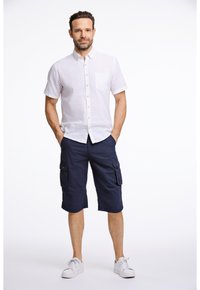 Valkoinen lyhythihainen nappipaita, jossa on rintatasku, yhdistettynä laivastonsinisiin cargo-shortsseihin, joissa on sivutaskut. Asusteena valkoiset tennarit.