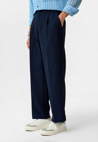 Marineblauwe geplooide broek met een streeppatroon, gemaakt van een textiele stof. In combinatie met witte sneakers, wat een ontspannen pasvormontwerp laat zien.