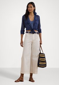 Chemise en voile bleu marine boutonnée à la taille, haut bleu clair en dessous, pantalon large crème, sandales marron à lanières, sac fourre-tout rayé.