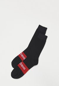 Calcetines negros con acentos de rayas rojas. Presentan texto blanco en la raya. Están hechos de una tela suave con una forma estándar de calcetín.