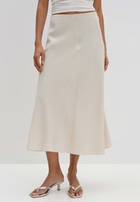 Jupe midi couleur crème en tissu texturé, avec une taille ajustée et un ourlet évasé, accompagnée de sandales à talons métalliques.