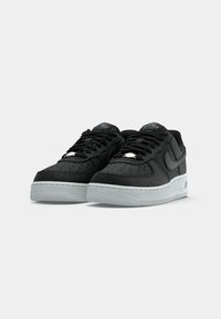 Muške crne tenisice s teksturiranim gornjim dijelom, bijelim srednjim dijelom i crnim vezicama. Sadrže Nike logotip i perforirani dizajn za prozračnost.