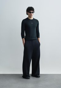 Čierny dlhý rukáv s priliehavým strihom a logom; voľné čierne nohavice; čierne slnečné okuliare; hladká štruktúra; minimalistický štýl a jednofarebná čierna.