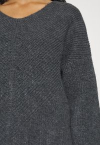 Pull en tricot gris foncé avec un col en V, un motif texturé et des manches côtelées, mettant en valeur un matériau doux ressemblant à de la laine.