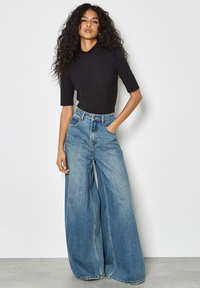Top nero a maniche corte abbinato a jeans in denim blu a gamba larga. I jeans presentano una vita alta, tasche anteriori e una texture sbiadita.