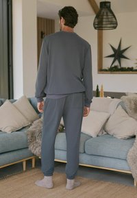 Grau meliertes Lounge-Set bestehend aus einem Langarmoberteil und elastischen Ankle-Pants. Weicher Stoff, lockere Passform, mit einer aufgesetzten Gesäßtasche.
