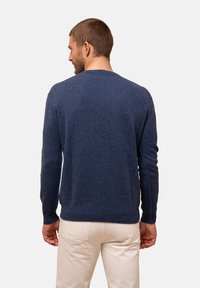 Granatowy sweter z miękkiej mieszanki wełny, okrągły dekolt, prążkowane mankiety i dół, noszony przez modelkę odwróconą tyłem na jednolitym tle.