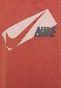 Punainen puuvillainen t-paita, jossa on suuri vaaleanpunainen Nike-swoosh ja musta "NIKE"-teksti, sileä pinta ja tavallinen pyöreä kaula-aukko.