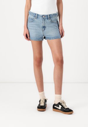 Lichte blauwe denim shorts met een rafelige zoom, gecombineerd met zwarte sneakers met een wit logo en beige veters, en crèmekleurige sokken.