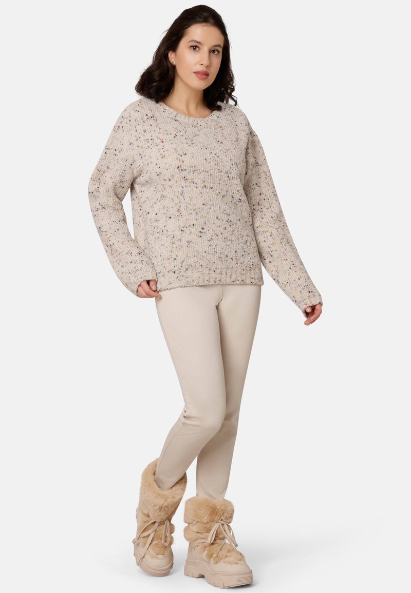 Strickpullover in Creme mit bunten Sprenkeln, entspannte Passform, lange Ärmel, kombiniert mit beigen Leggings und beigen, fellgefütterten Stiefeln.
