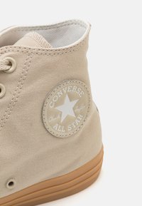Sneaker de cano alto em tela bege com sola de borracha, apresentando um emblema redondo com uma estrela e texto, e atacadores tonais.