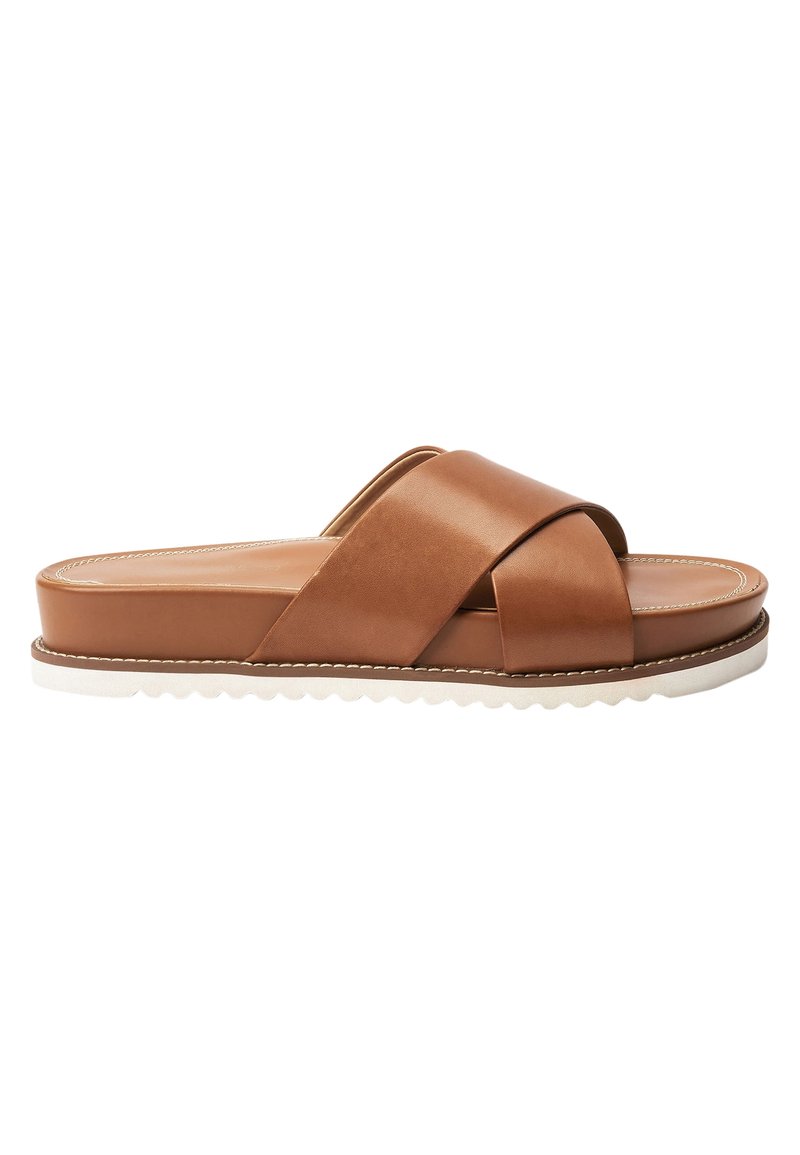 Bruine leren slipper met kruislings gespen, een gestructureerde witte zool en een plat ontwerp. Heeft een gladde afwerking en gestikte details.
