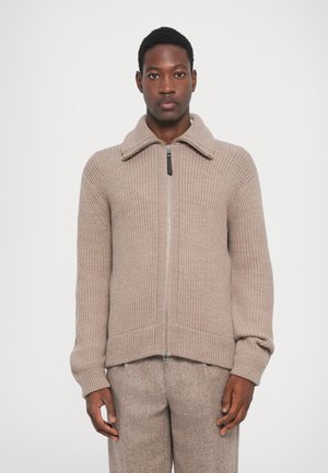 Cardigan beige à fermeture éclair avec texture côtelée, col large, manches longues et ourlet droit. Il dispose d'une fermeture éclair en argent et d'une coupe décontractée.