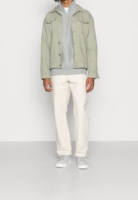 Chaqueta de denim verde claro sobre un sudadero con capucha gris, combinado con pantalones color crema y zapatillas gris claro. Diseño simple y casual.
