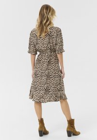 Leopardmönstrad klänning i lätt tyg med korta ärmar, åtsittande midja och utsvängd kjol, matchad med bruna ankelstövlar.