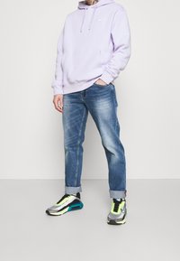 Ljuslila huvtröja med framficka, kombinerad med ljusblå, löst sittande jeans och grå, svarta och neongröna sneakers.