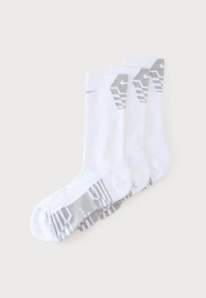 Trois paires de chaussettes blanches montantes avec un swoosh Nike gris et des motifs rayés, empilées sur un fond clair.