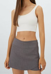 Witte geribde crop top met brede bandjes, gecombineerd met een grijze wikkel minirok met een soepele textuur en diagonale zoom.
