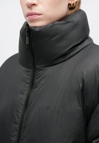 Čierna zateplená bunda s vysokým golierom, zipsovým zapínaním a hladkou, lesklou textúrou. Obsahuje jemné logo na oblasti hrudníka.