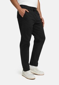 Black cotton pants with pockets and a smooth texture, paired with white sneakers featuring a beige sole and light accents.