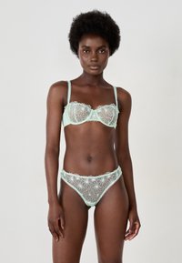 Mintgrünes Dessous-Set bestehend aus einem transparenten BH mit floralen Stickereien und passenden hochgeschnittenen Panties mit Spitzenbesatz und gewellten Kanten.