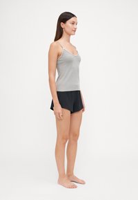 Débardeur gris côtelé avec fines bretelles associé à un short noir. Le débardeur a un décolleté en V et une silhouette ajustée. Texture lisse.