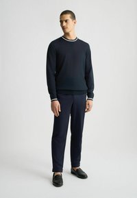 Jersey de naví con cuello a rayas en blanco y gris, combinado con pantalones de naví y mocasines negros. Textura suave, diseño ajustado.