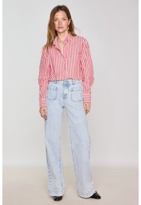 Camicia a righe rossa e bianca con taschino sul petto, abbinata a jeans in denim azzurro chiaro a gamba larga con due tasche posteriori.