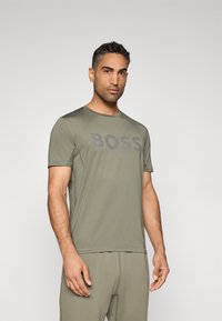 T-shirt verde-oliva de manga curta com decote redondo, apresentando um logótipo "BOSS" em destaque numa tonalidade mais escura. Tecido suave e design ajustado.