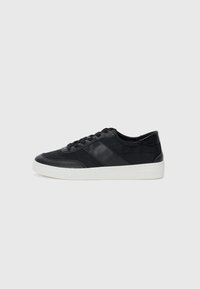Zwarte leren sneaker met een witte rubberen zool, voorzien van textuurpanelen en vetersluiting. Minimalistisch ontwerp zonder zichtbare merkvermeldingen.