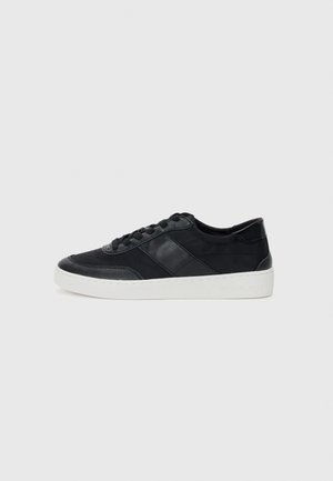 Baskets en cuir noir avec une semelle en caoutchouc blanc, dotées de panneaux texturés et d'une fermeture à lacets. Design minimaliste sans marquage visible.