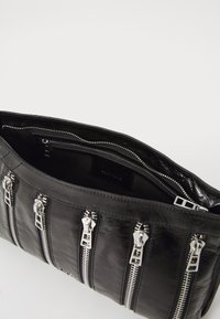 Sac en cuir noir avec plusieurs compartiments zippés et quincaillerie argentée. Texture lisse avec un design épuré. Poche intérieure visible.