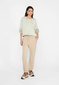 Heleroheline lühikese lõikega kapuutsiga dressipluus paelaga ja esitaskuga, koos beežide paelaga pükstega. Pruunid tossud valgete detailidega.