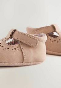 Chaussures pour tout-petits rose clair en daim doux, avec des motifs découpés et une sangle Velcro, dotées d'une doublure textile florale et d'une forme arrondie.