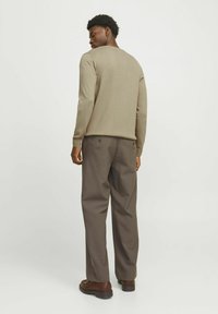 Beige Pullover mit langen Ärmeln und rundem Halsausschnitt. Kombiniert mit braunen Hosen, die seitliche Taschen und Knöpfe haben. Glatte Textur, figurbetonter Schnitt.