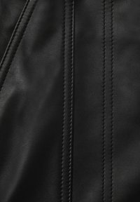 Material de cuero negro con una textura suave, que presenta costuras prominentes y un ligero brillo. Diseño sin patrones y forma clásica.