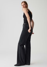 Jean flare en denim noir à taille haute, avec un design classique à cinq poches et des détails de couture subtils, associés à un débardeur noir.