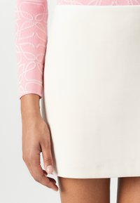 Witte mini-jurk met een gladde textuur, gecombineerd met een roze lange mouw top met een lichte bloemenpatroon op de mouwen.