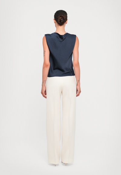 Marineblaues ärmelloses Oberteil mit glatter Textur, kombiniert mit hochwaistigen, weit geschnittenen weißen Hosen. Das Outfit hat ein minimalistisches Design.