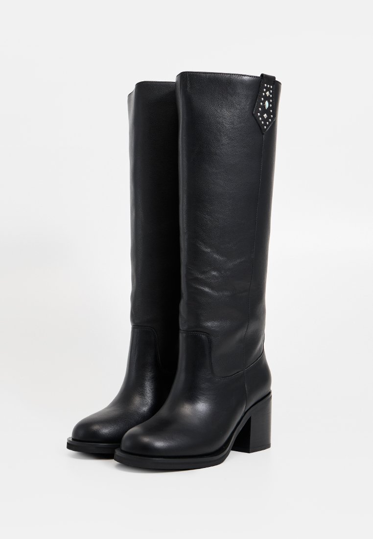 Bottes en cuir noir montantes avec un talon carré, présentant une finition texturée et un accent décoratif clouté sur le bord supérieur.