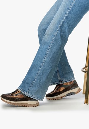 Person wearing blue jeans and brown textured sneakers with thick beige soles, sitting on a metallic gold stool.