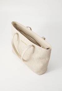Cream-colored tote bag made of textured material, featuring embossed logo design, dual handles, and zippered interior compartment.