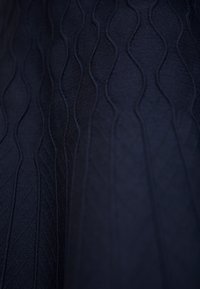 Tissu texturé bleu marine foncé présentant des motifs ondulés et de subtils motifs de diamants, avec une texture lisse et douce qui renforce sa profondeur visuelle.