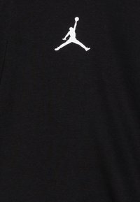 Camiseta de jersey negra con un logo Jumpman blanco en el pecho. La tela tiene una textura suave y un diseño de cuello redondo.