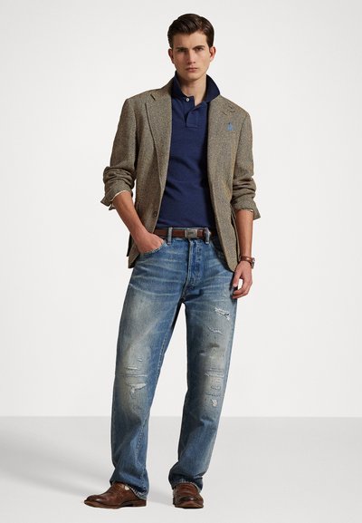 Brun rutete blazer over marinblå polo, kombinert med slitte blå jeans og brune skinnboots. Merkbar slitasje på jeans med synlige riftmønstre.