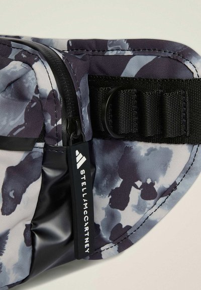 Zbliżenie na torebkę z tkaniny w czarno-szary wzór, z zamkiem błyskawicznym, czarnymi pętlami do paska oraz metką z napisem "Stella McCartney".