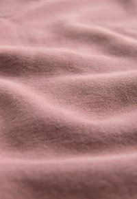 Zacht roze stof met subtiele plooien en fijne gebreide textuur, die zachte golven en een glad oppervlak toont.